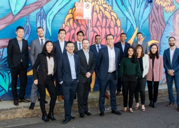 Group of professionals standing on street with colourful wall graffiti behind them